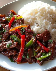 A bowl of crispy chili beef served with rice, garnished with vegetables.